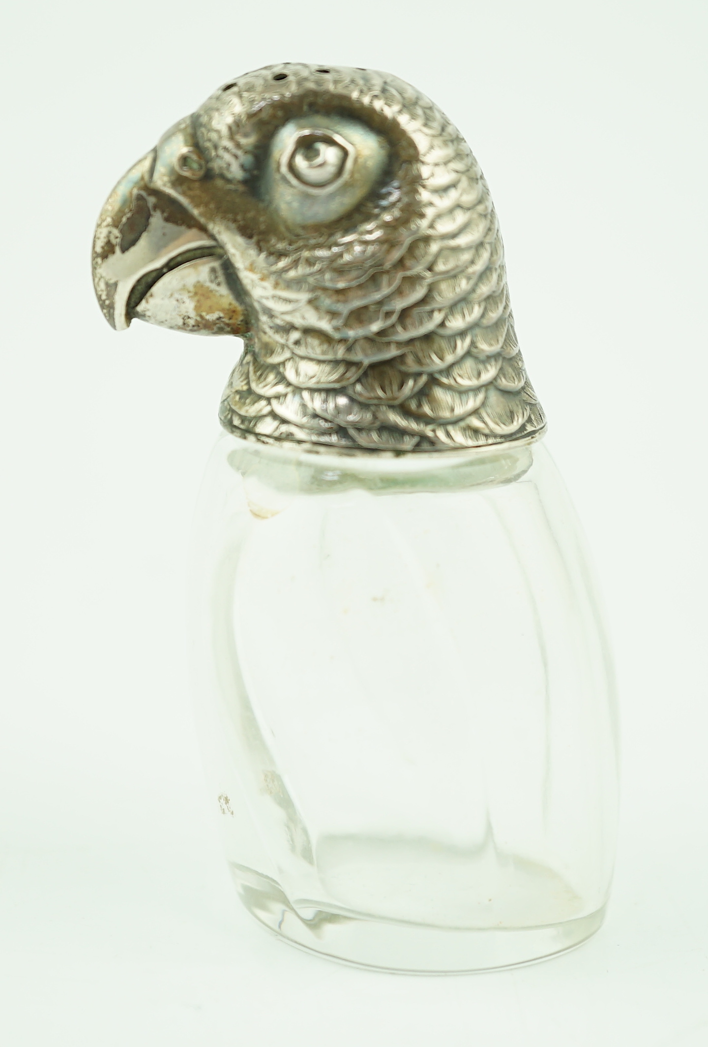 An early 20th century German 800 standard silver mounted glass pepperette, the cover modelled as the head of a parrot